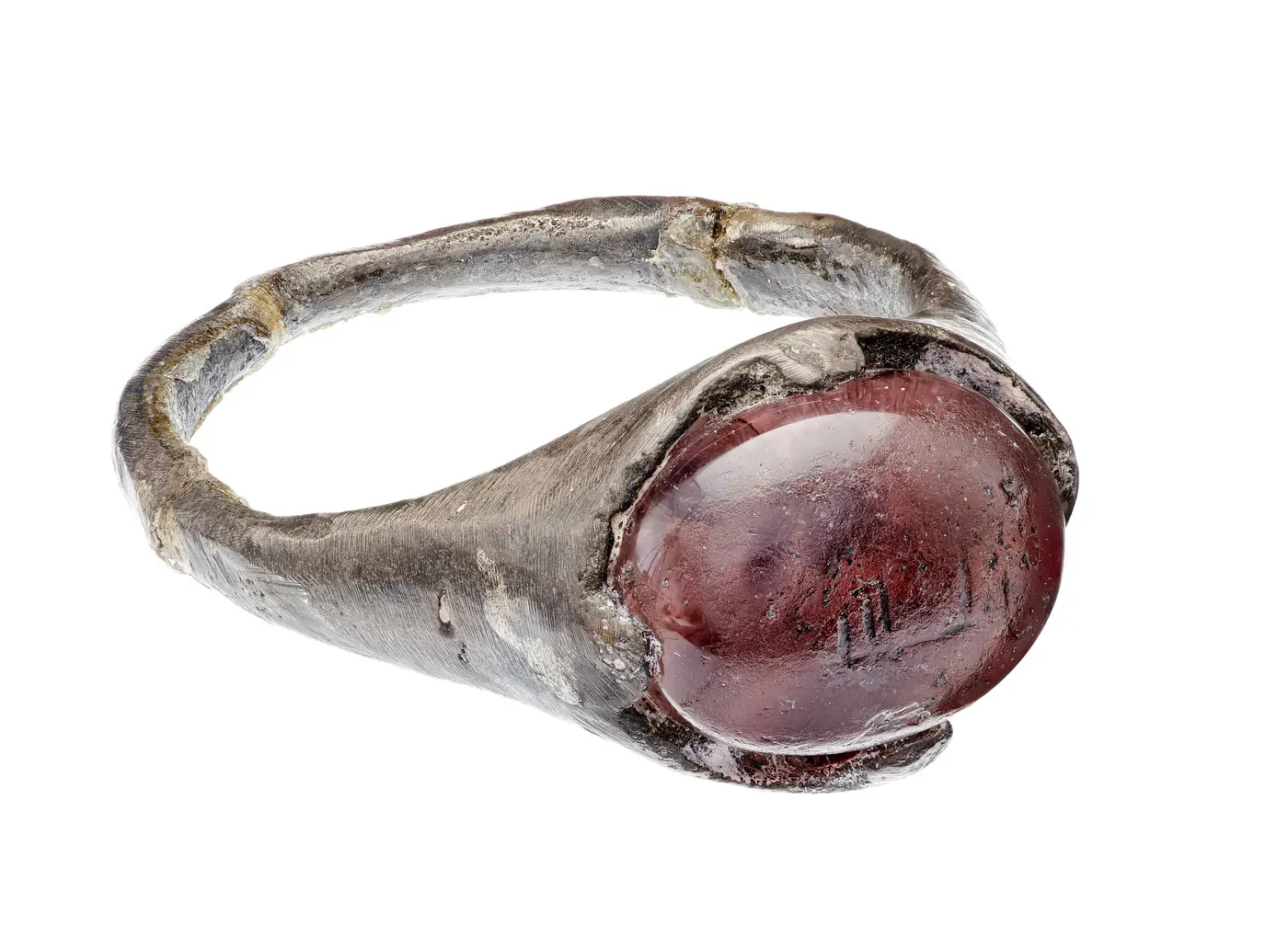 Silverring med en oval, violett glassten i vilken tecken är inristade, fotograferad mot vit botten.
