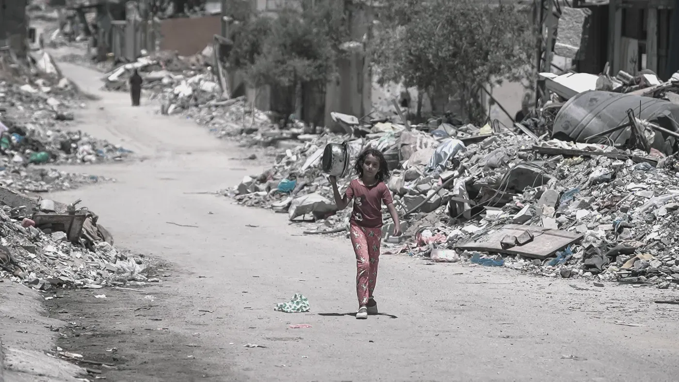 En flicka i rosa går ensam på en gata i Gaza med rasmassor och skräp på båda sidor.