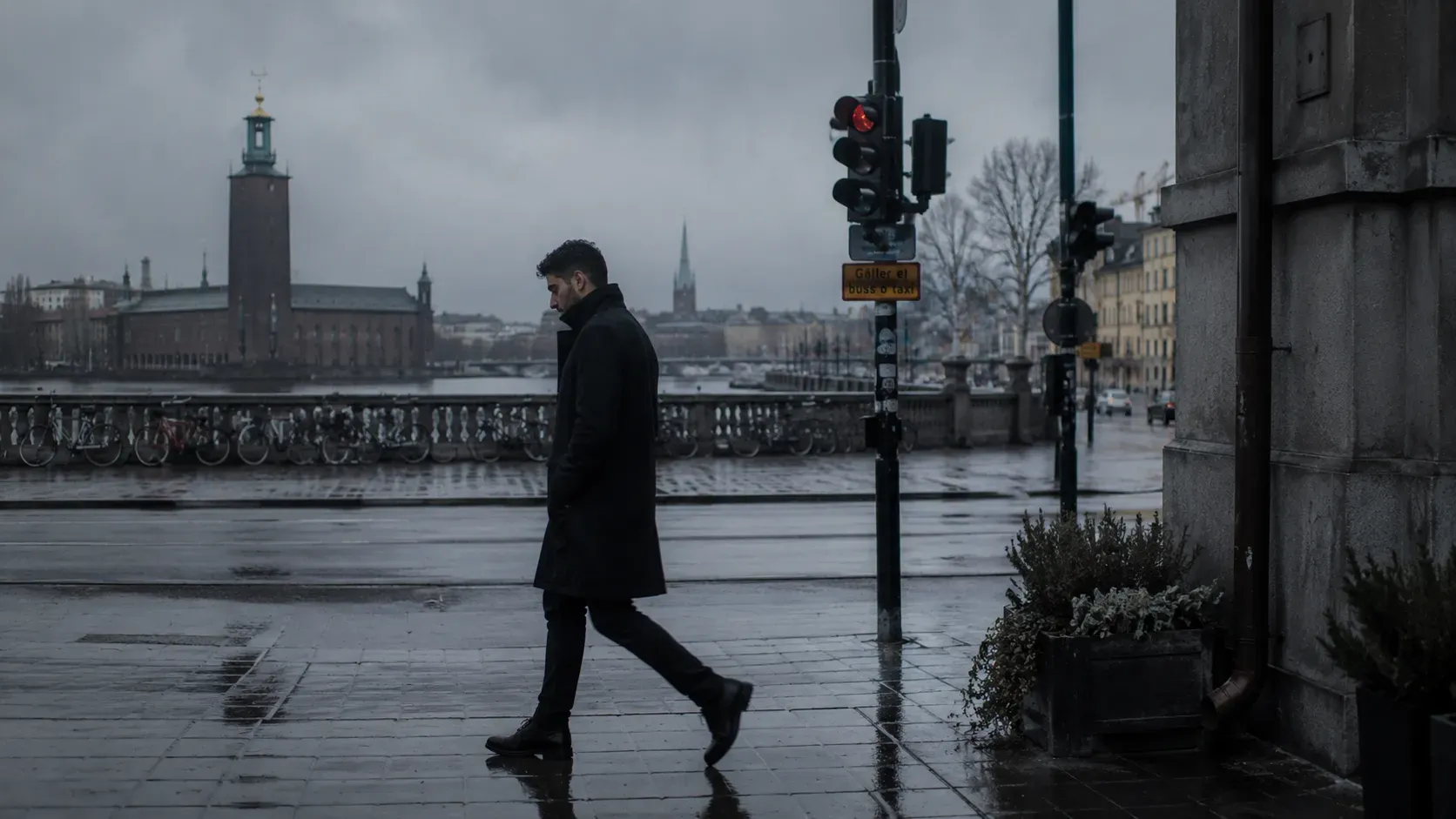 Ensam man i svart rock går längs en regnvåt Stockholmskaj med Stadshusets torn och Riddarholmskyrkans spira i grå fjärran.