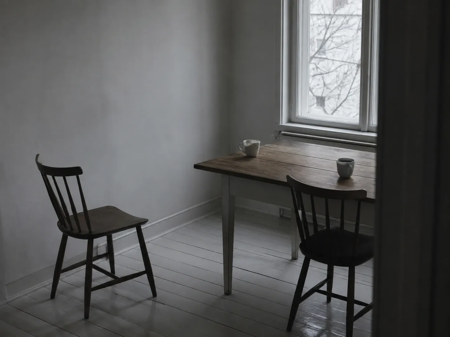 Köksbord vid ett fönster med två koppar i var sin ände och en stol utdragen från bordet